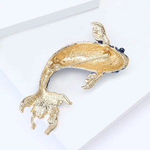 Detail view of goldfish brooch with hammered gold texture and blue enamel accents