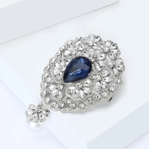 Detail einer Vintage-Blumenbrosche mit tiefblauem Edelstein und hängender weißer Perle