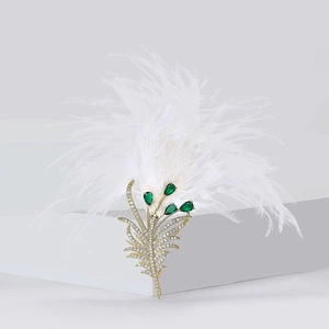 Detailed close-up of luxury gold feather brooch with green gems and white ostrich feathers