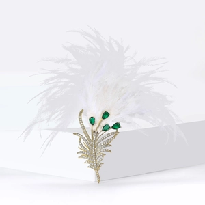 Luxurious feather brooch with sparkling zircons and green gems on white pedestal