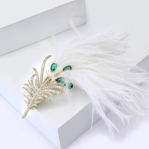 Detail view of gold feather brooch with green pear-cut stones and white feathers