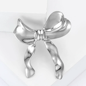 Broche nœud en métal liquide argenté poli sur un piédestal blanc minimaliste