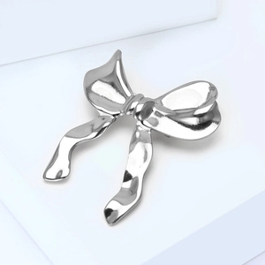 Détail de la broche nœud argentée montrant la texture du métal martelé sur un support blanc