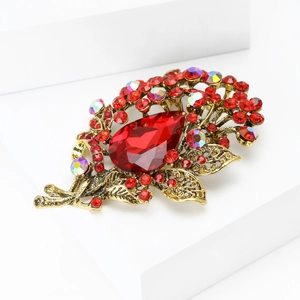 Detail view of vintage gold-toned brooch with large red teardrop crystal and leaf design