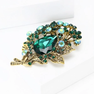 Macro detail of vintage gold brooch featuring large green pear-cut gemstone and crystals