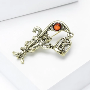 Detail of vintage gold cat and birdcage brooch with amber stone on white podium