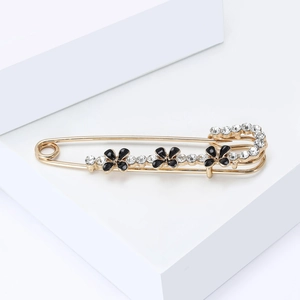 Détail d'une broche épingle dorée avec fleurs de trèfle noires et cristaux étincelants