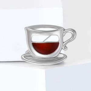 Détail d'une broche tasse à café argentée avec émail rouge sur un support blanc