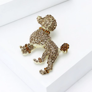 Détail de la broche caniche dorée avec strass ambrés sur un support minimaliste