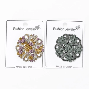 Detailed close-up of crystal wreath brooches in gold and gunmetal finish on display card