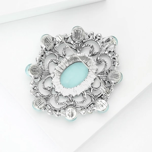 Vue détaillée d'une broche baroque avec cabochon bleu clair et motifs argentés ajourés complexes