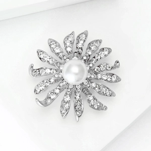 Vue macro de la broche fleur argentée ornée d'une perle centrale et de strass brillants