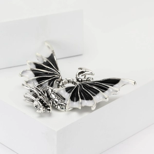 Detail shot of silver dragon brooch featuring intricate black and white enamel wings