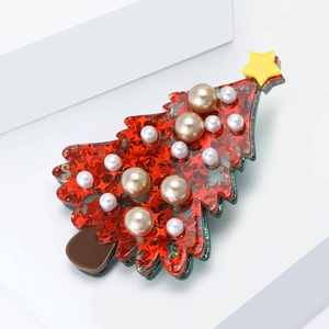 Red acrylic Christmas tree brooch with star sequins and pearls on white podium