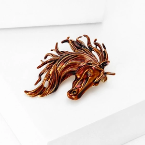 Detail of horse head brooch with brown enamel finish and polished golden metal alloy texture