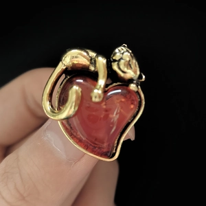Detailed macro view of a golden cat climbing a heart-shaped amber gemstone on a ring