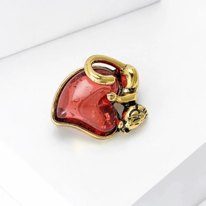Detailed macro of vintage gold alloy monkey embracing a ruby red resin heart brooch