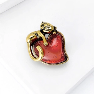 Detailed macro view of a cute golden cat brooch lying on a textured red enamel heart