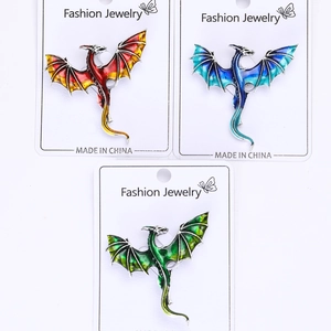 Three vibrant enamel flying dragon brooches in red, blue, and green on display cards