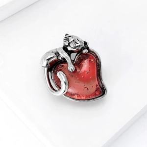 Close-up of a silver cat brooch resting on a translucent red heart gemstone