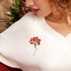 Close-up of red rhinestone carnation brooch with enamel leaves and a white pearl drop