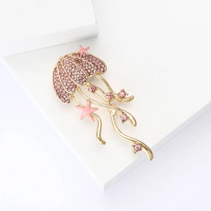 Detail of a gold jellyfish brooch with pink rhinestones and enamel starfish on a white base