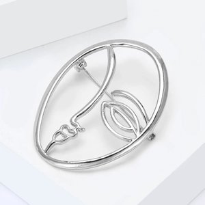 Detailed view of silver minimalist abstract face brooch on white geometric props