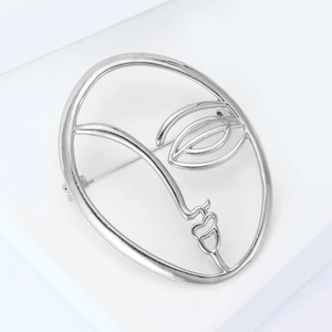Artistic silver abstract face brooch with hollow metal lines on a minimalist pedestal