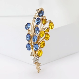 Dettaglio macro di una spilla a bouquet dorata con cristalli blu e accenti micro-pave