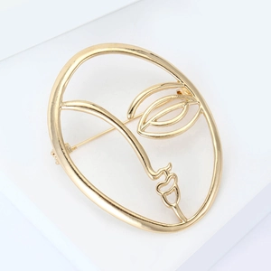 Macro detail of a minimalist golden abstract face brooch with a smooth polished finish