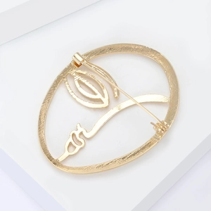 Macro detail of a minimalist gold face profile brooch with abstract lines on a clean background
