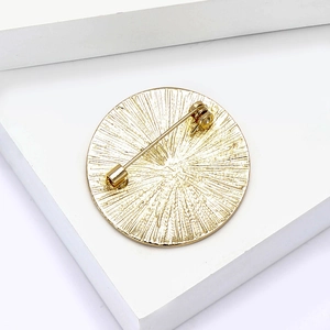 Detail showing the golden metal brooch back with radial texture and secure pin mechanism