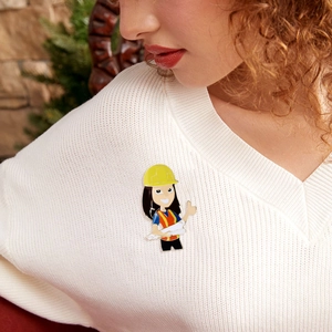 Detail of cartoon female engineer enamel pin featuring a hard hat on a white sweater