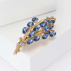 Dettaglio ravvicinato di una spilla a forma di grano dorato con cristalli blu e piccoli strass