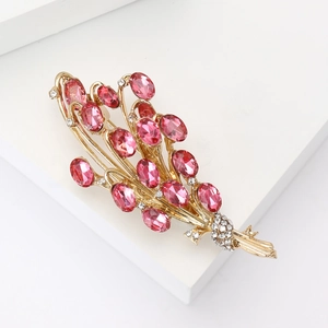 Dettaglio macro della spilla spiga dorata con gemme rosa viola e accenti di zircone