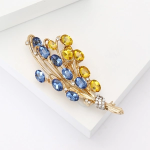Dettaglio spilla a spiga dorata con cristalli blu e gialli e zirconi micro-pavé