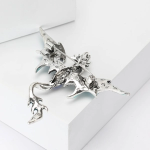 Detail view of the silver dragon brooch showing wings texture and safety pin clasp back