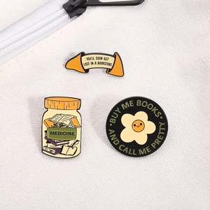 Three enamel book pins set on white canvas bag including floral and jar designs