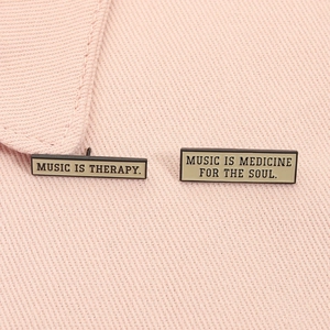 Detail of Music is Therapy enamel pins pinned on pink fabric showing fine metal texture