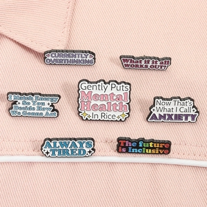 Macro shot of 7 enamel pins with mental health slogans pinned on pink denim fabric