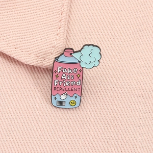 Détail d'un pin's émaillé rose avec texte Fake Ass Friend Repellent sur du denim rose