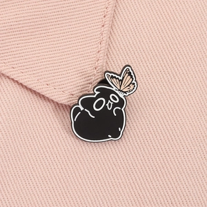 Close-up of a cute black cartoon ghost and orange butterfly enamel pin on pink fabric