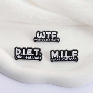 Set mit 3 humorvollen Emaille-Pins mit lustigen Food-Akronymen auf einem Display-Tablett