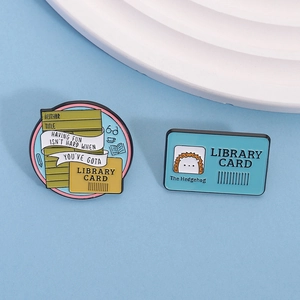 Detail of library theme enamel pins with hedgehog and book card on blue background