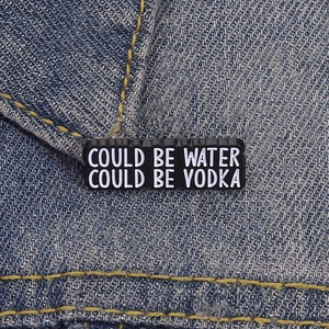 Detail of funny enamel pin with quote COULD BE WATER COULD BE VODKA on blue denim jacket