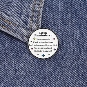 Close-up of a Little Reminders round white enamel pin badge pinned on blue denim fabric