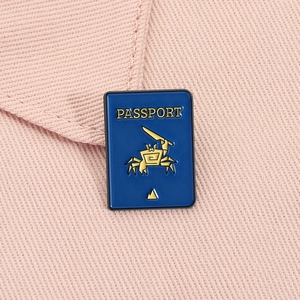 Detail of blue passport enamel pin with a golden crab and knife on pink fabric