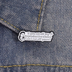 Cartoon feminist enamel pin with empowering text on blue denim fabric background
