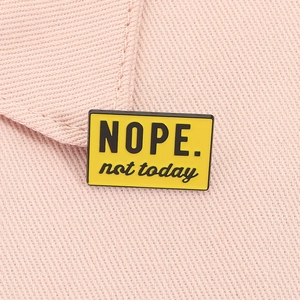 Detailed macro view of yellow enamel pin featuring Nope Not Today text on pink fabric