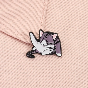 Close-up of a cute purple striped cat enamel pin showing funny licking pose on pink fabric